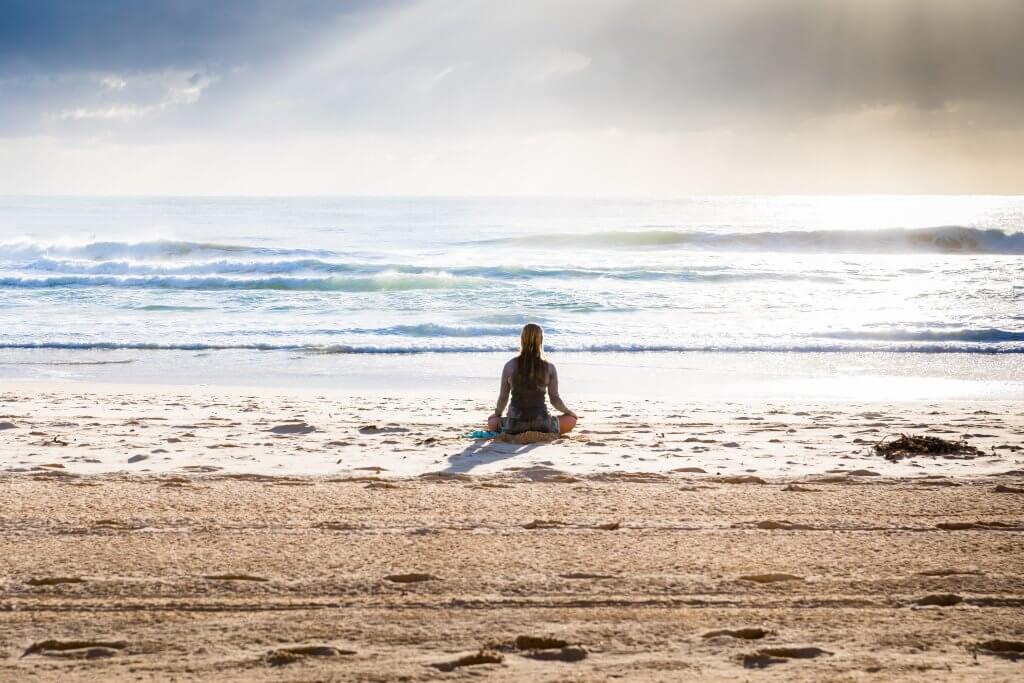 woman meditating on the beach - best yoga shoes