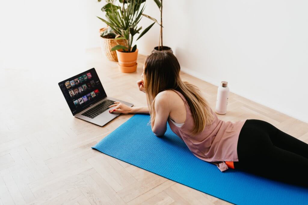 woman lying on yoga mat with computer - best yoga teacher training online