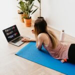 woman lying on yoga mat with computer - best yoga teacher training online
