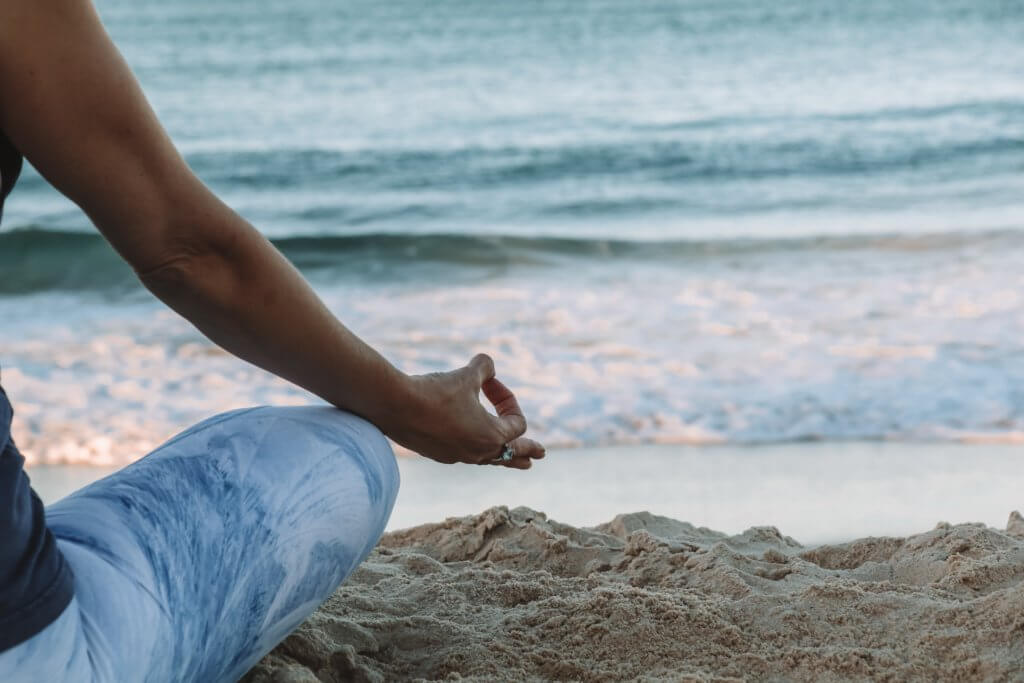 woman meditating on the beach - best yoga retreats in Europe