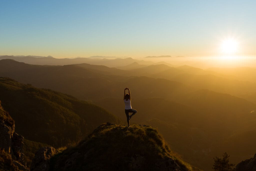 woman practicing yoga on top of a mountain - best yoga retreats in Europe