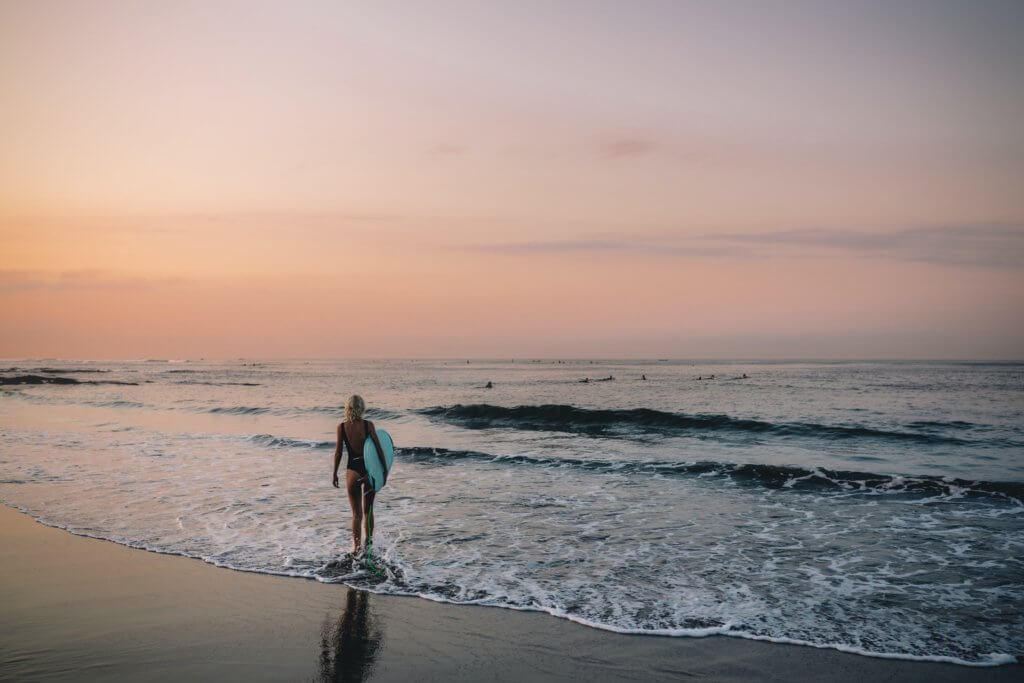 woman with surfboard on Canggu beach - best surf and yoga retreats in Bali